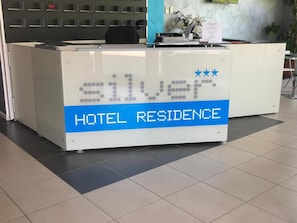 A reception desk with a digital display indicating 'HOTEL RESIDENCE' and a logo with three stars.
