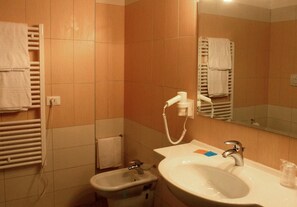 Een badkamer met een wastafel, spiegel, handdoekhouder en een losse haardroger.