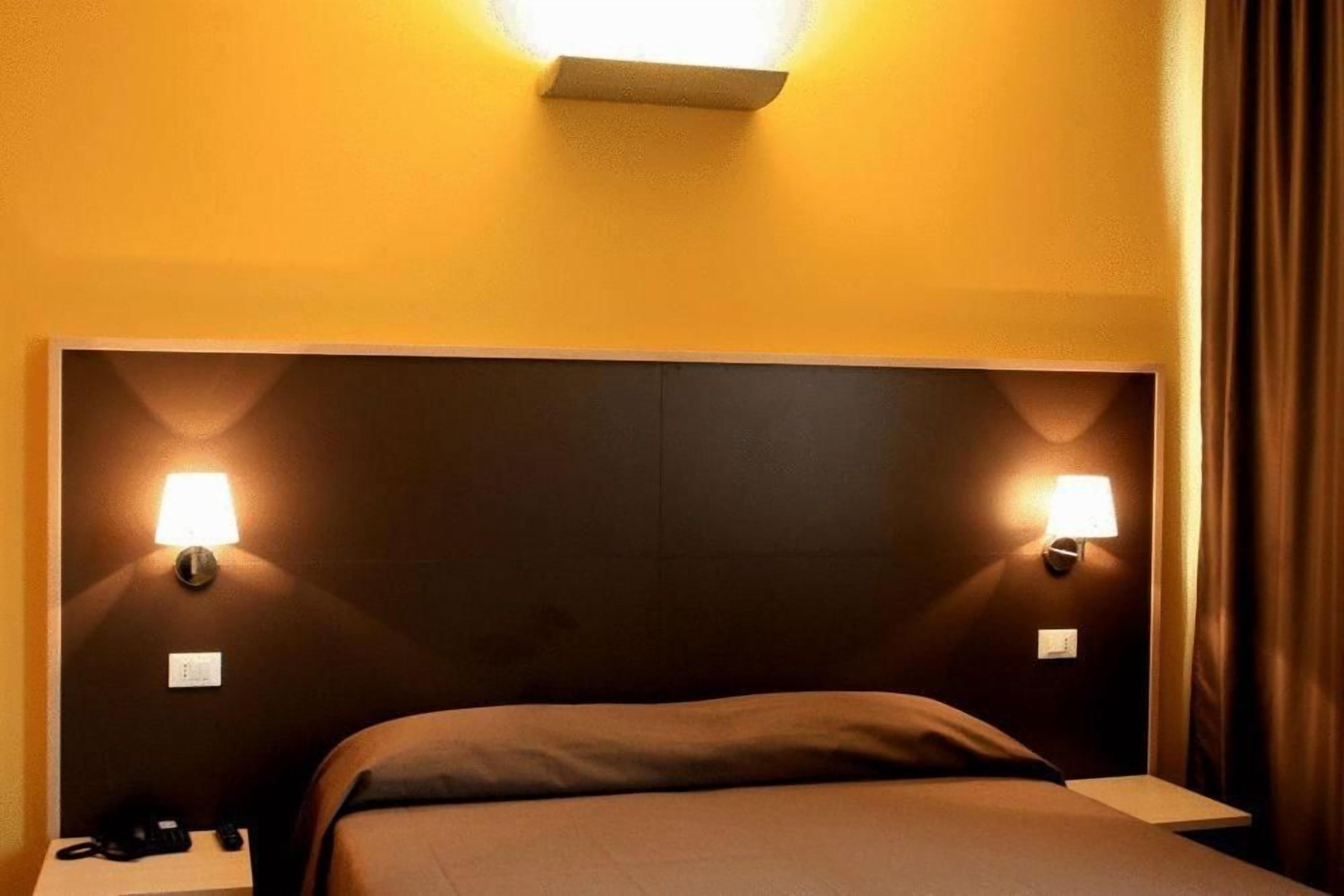 Una camera d'albergo con un letto grande, due lampade ai comodini e un comodino con un telefono.