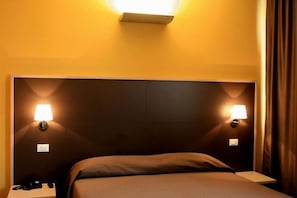 A hotel room with a large bed, two bedside lamps, and a nightstand with a phone.