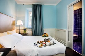 Een hotelkamer met een bed, een dienblad met ontbijtartikelen, een lamp en een raam met gordijnen.
