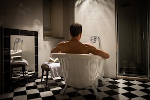 Een badkamer met een geruite vloer, een bad, een spiegel en een handdoekhouder.