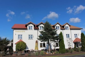 A multi-story building with a red roof, white walls, and a visible entrance with a yellow door.