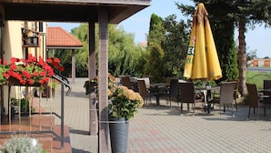 An outdoor patio area with tables and chairs, a covered seating area, and potted plants. - Restauracja Hotel Kassandra (Września)