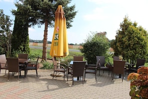 An outdoor seating area with wicker chairs and a yellow umbrella, surrounded by trees and a view of a road.