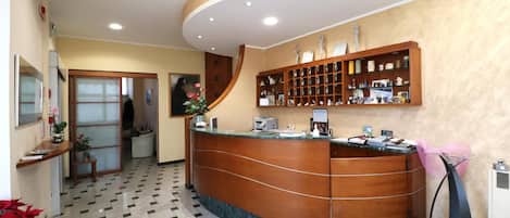 Un área de recepción con mostrador de madera curvo, piso de baldosas y una vitrina empotrada en la pared.