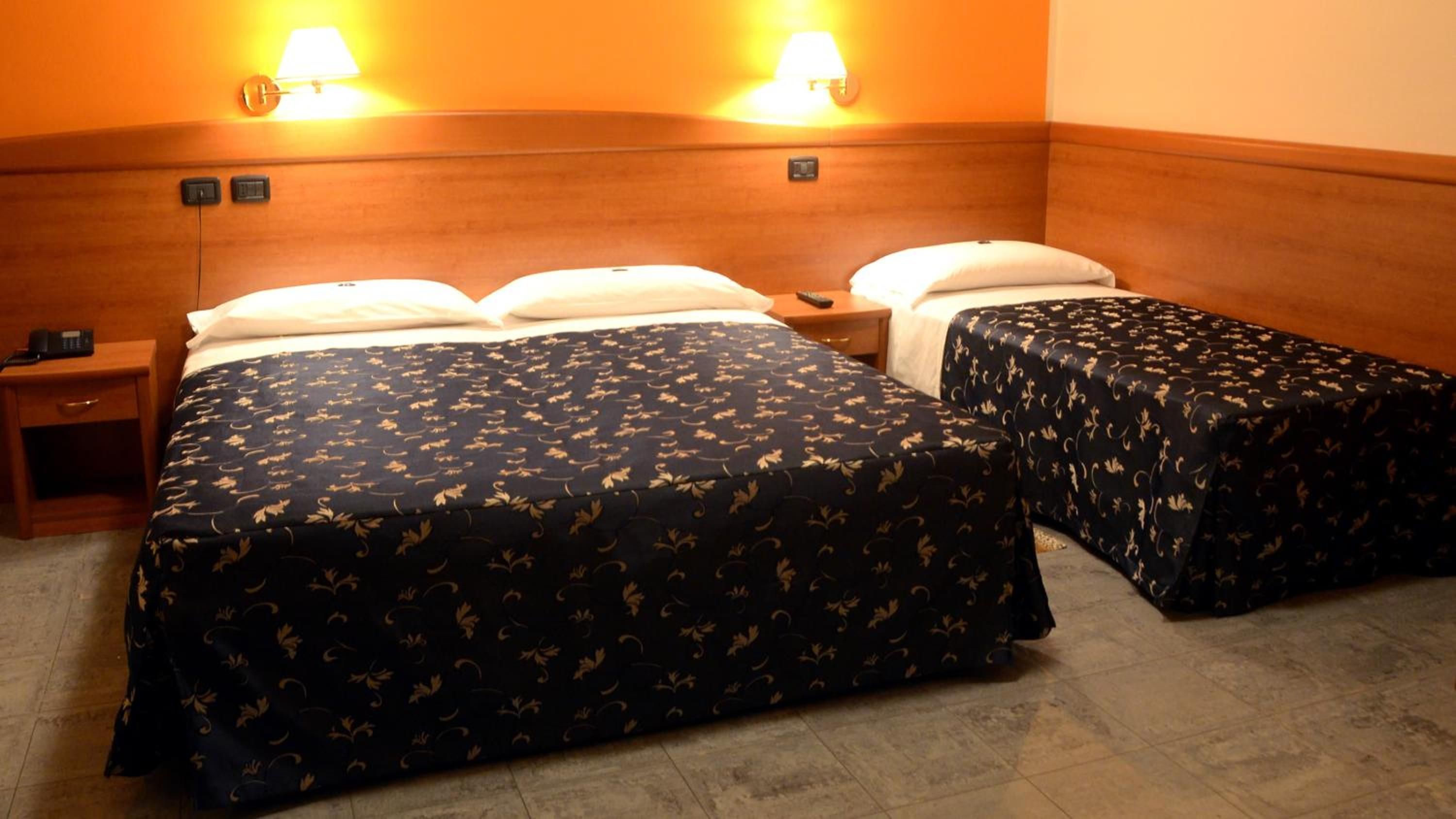 A hotel room with two beds, a nightstand, and a lamp.