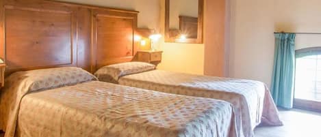 Camera d'albergo con due letti, una testiera in legno, lampade sui comodini, una scrivania e una finestra con tende.