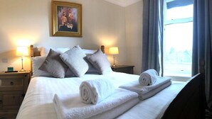 Una habitación de hotel con una cama, dos lámparas de noche, una mesita de noche, una ventana con cortinas y un cuadro en la pared.