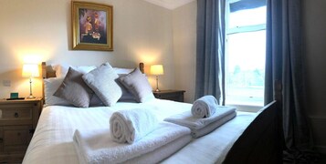A hotel room with a bed, two bedside lamps, a nightstand, a window with curtains, and a painting on the wall.