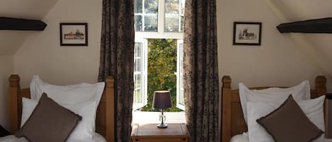A bedroom with two beds, a window with curtains, a nightstand with a lamp, and two framed pictures on the wall.
