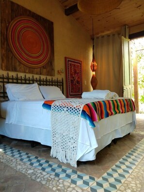 A bedroom with a bed, a patterned wall hanging, a decorative wall piece, and a patterned floor. - Zazen Pousada By Santoregano (Maceió)