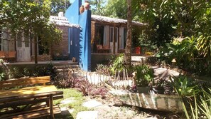A courtyard with a wooden bench, a blue wall, and a small building with a tiled roof. - Zazen Pousada By Santoregano (Maceió)