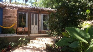A rustic building with a wooden door, a small porch with chairs, and a yellow rope barrier. - Zazen Pousada By Santoregano (Maceió)