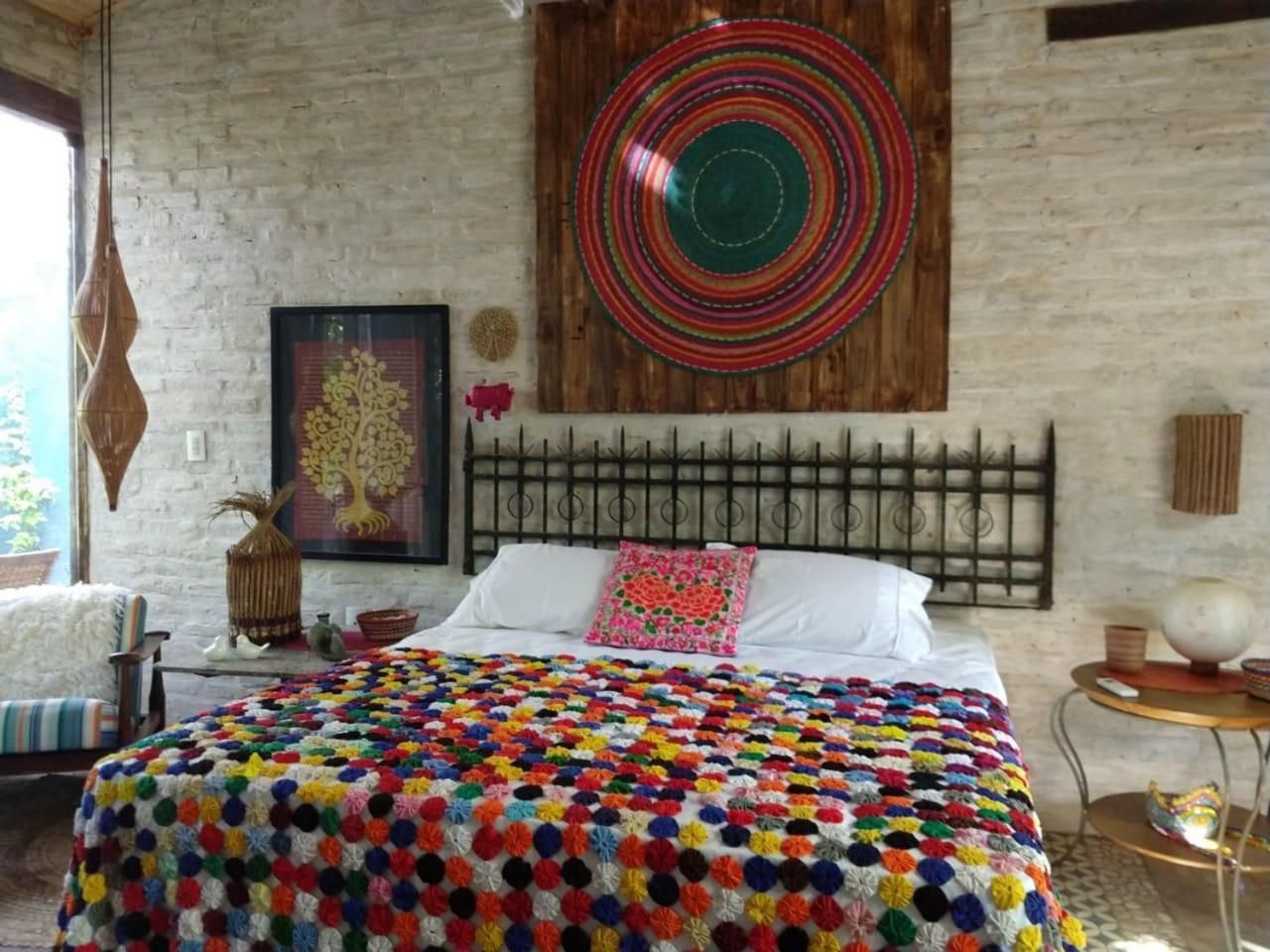 Un dormitorio con una cama grande, un edredón colorido, una pared de madera, un cabecero de metal y un adorno circular en la pared.
