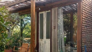 A covered porch with a wooden door, two wicker chairs, and a potted plant. - Zazen Pousada By Santoregano (Maceió)