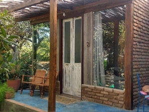 A covered porch with a wooden door, two wicker chairs, and a potted plant. - Zazen Pousada By Santoregano (Maceió)