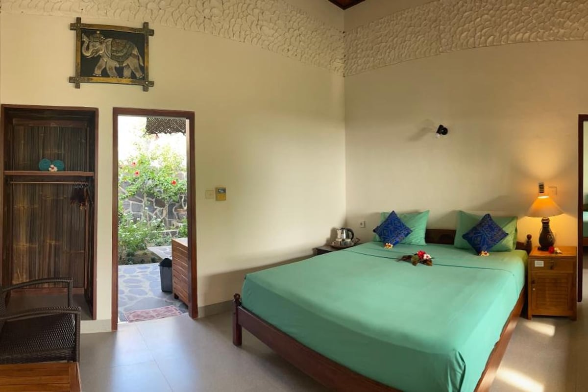Un dormitorio con cama, mesitas de noche, lámpara y vistas al exterior.