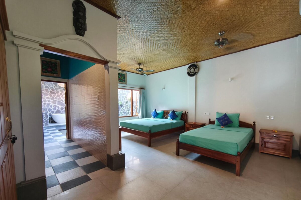Habitación de hotel con dos camas, piso a cuadros, pared de piedra y vista a un edificio de piedra.