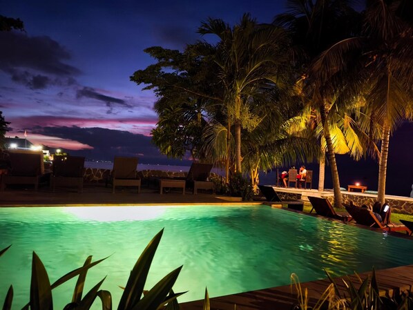 A nighttime pool area with lounge chairs and palm trees.