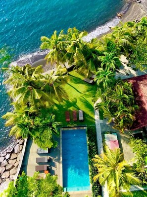 Vista aérea de un resort con piscina, tumbonas y playa.
