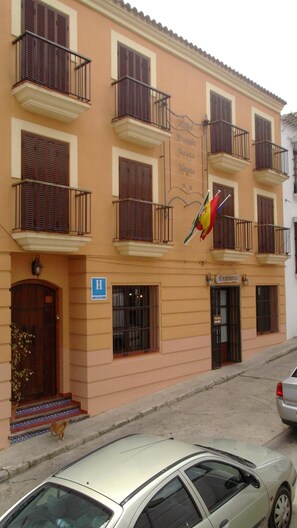 Un edificio de hotel con varios balcones, un letrero que indica que es un hotel, y una entrada visible con una puerta y escalones.