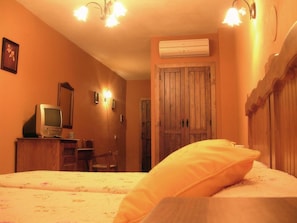 Una habitación con cama, televisión sobre una cómoda de madera, aire acondicionado y una puerta.