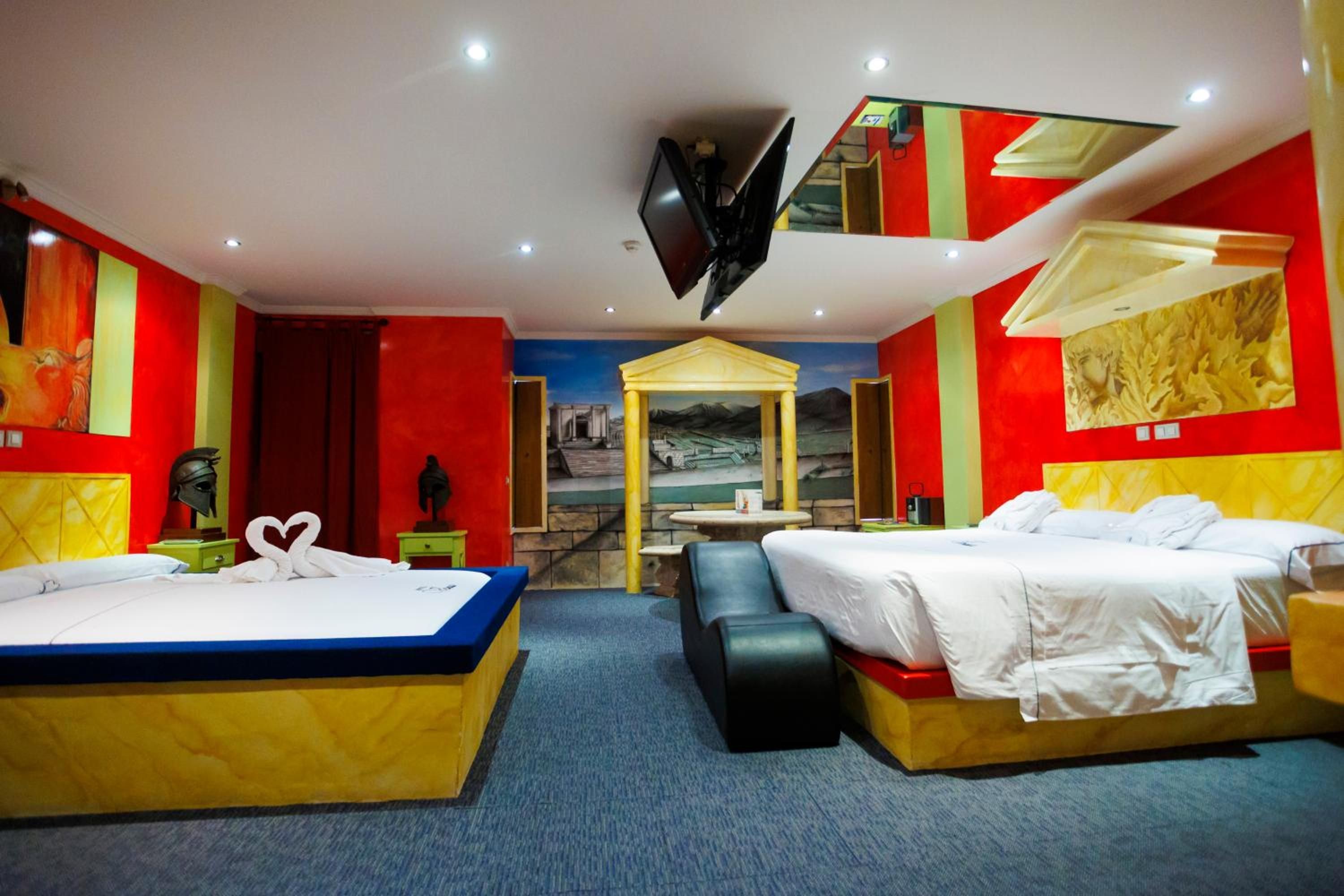 A hotel room with two beds, a TV, a mural, and a small table.