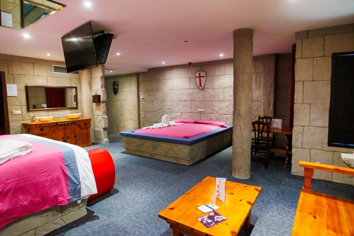 Habitación de hotel con una cama, un aparador de madera, un televisor y una pared de piedra.