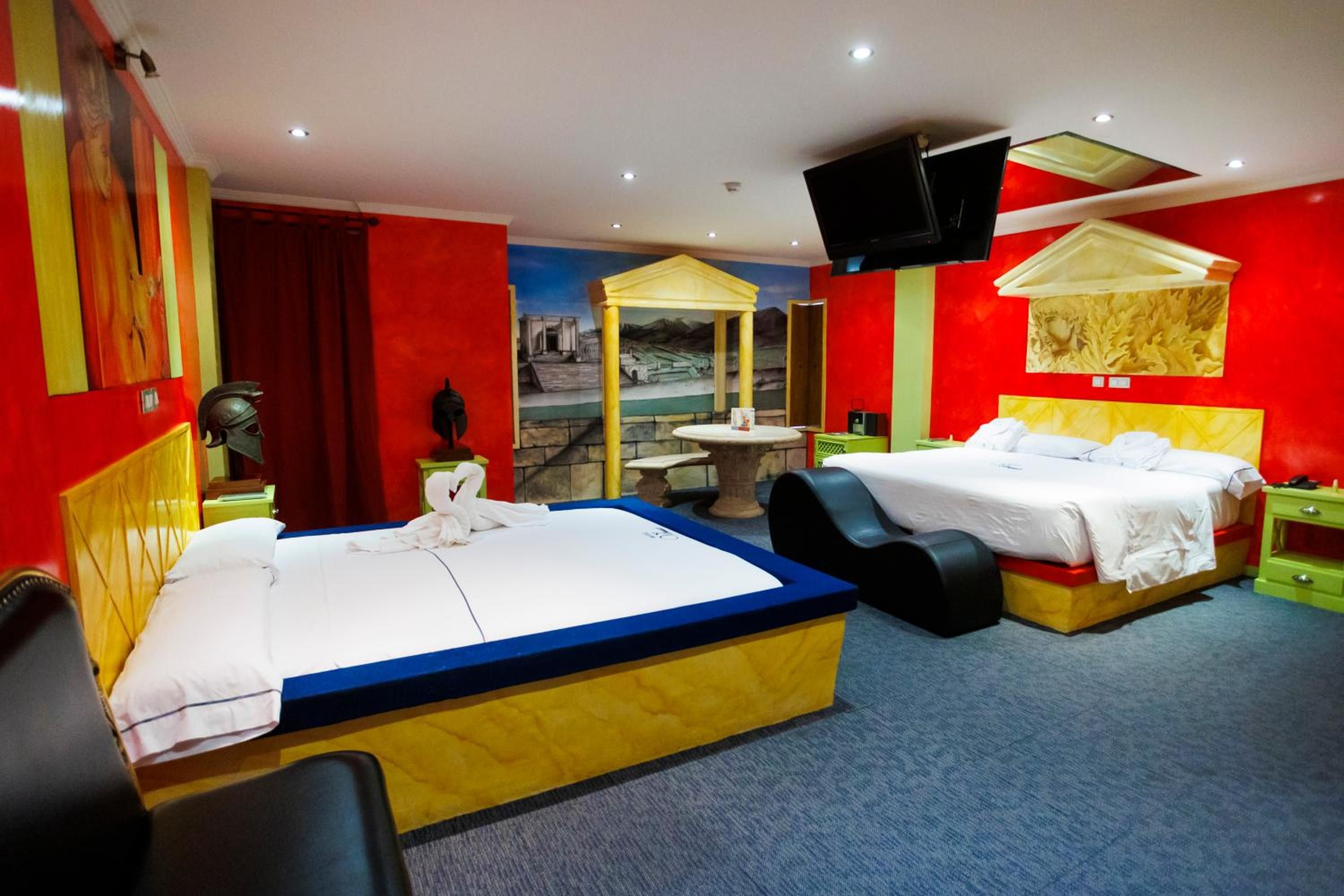 A hotel room with two beds, a small table, a TV, and a mural on the wall.