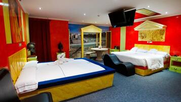 A hotel room with two beds, a small table, a TV, and a mural on the wall.