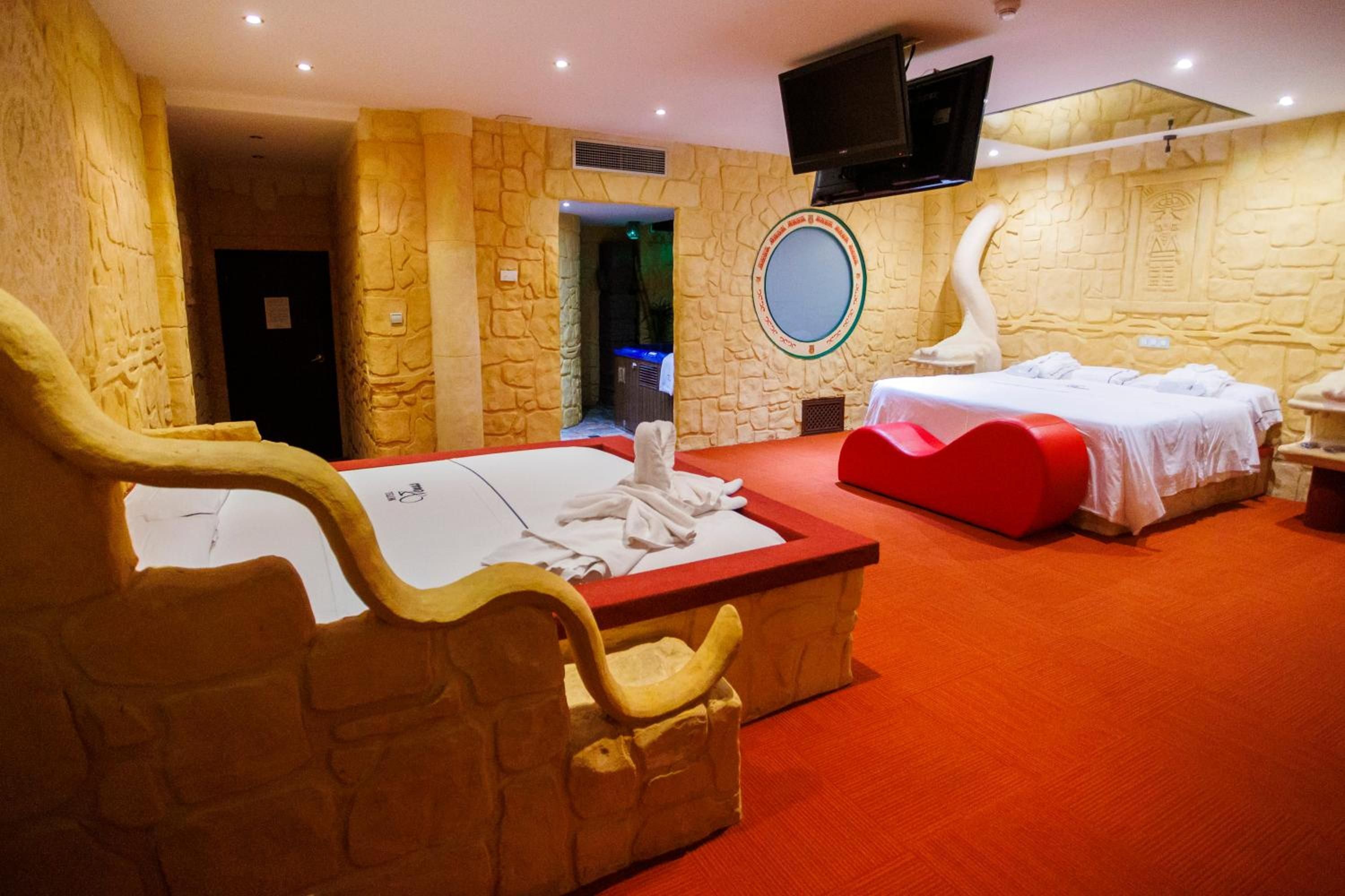 Habitación de hotel con pared de piedra, una cama grande, una cama más pequeña, un televisor montado en la pared y una alfombra roja.