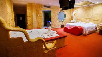 Habitación de hotel con pared de piedra, una cama grande, una cama más pequeña, un televisor montado en la pared y una alfombra roja.