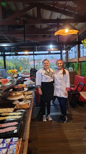 Two individuals in a restaurant with a variety of desserts on display. - Pousada Praia Brava (Matinhos)