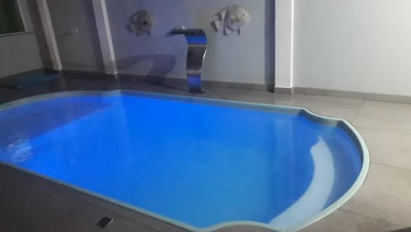 An indoor swimming pool with a blue interior, a tiled floor, and a wall-mounted faucet.