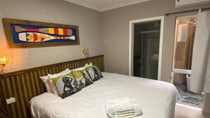 A hotel room with a bed, pillows, a wall art piece, a bedside table, and a window. - Pousada Praia Brava (Matinhos)