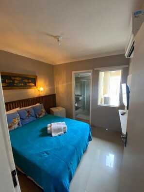 Habitación de hotel con cama, mesita de noche, lámpara de pared, ventilador de techo, zona de ducha y ventana.