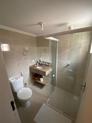 Un baño con inodoro, lavabo, cabina de ducha de vidrio y espejo.