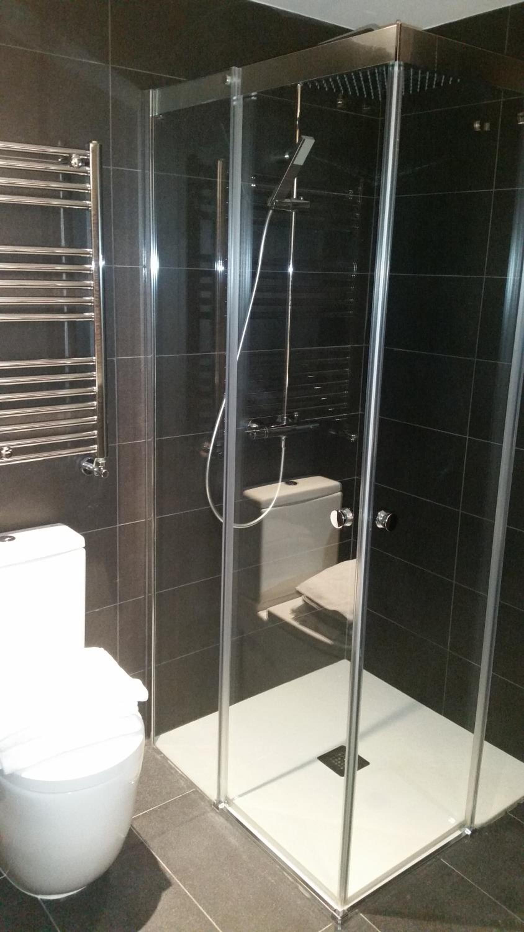 A modern bathroom with a glass-enclosed shower, a toilet, and a towel rack.