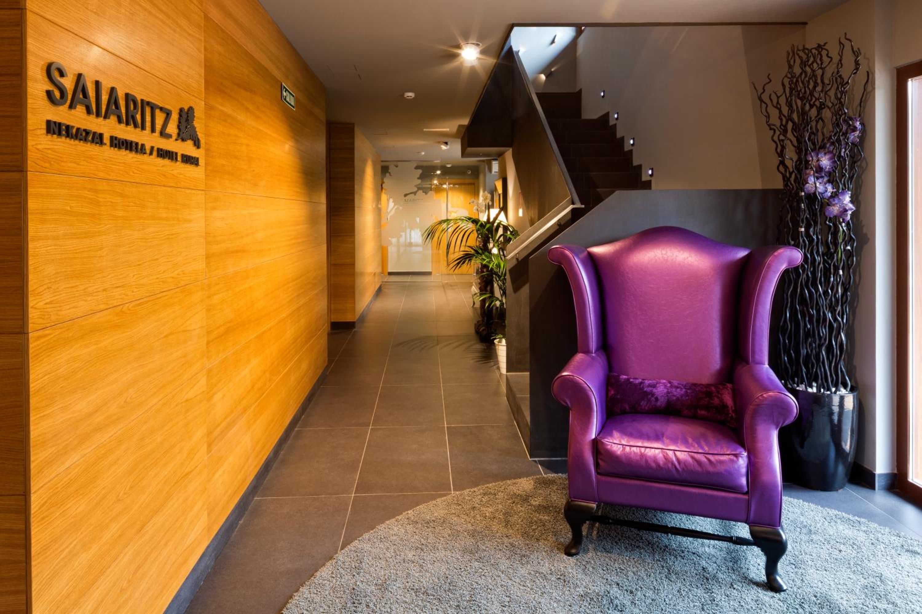 Um hall de hotel com parede de madeira, uma poltrona roxa e uma escadaria.