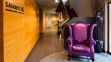 Um hall de hotel com parede de madeira, uma poltrona roxa e uma escadaria.
