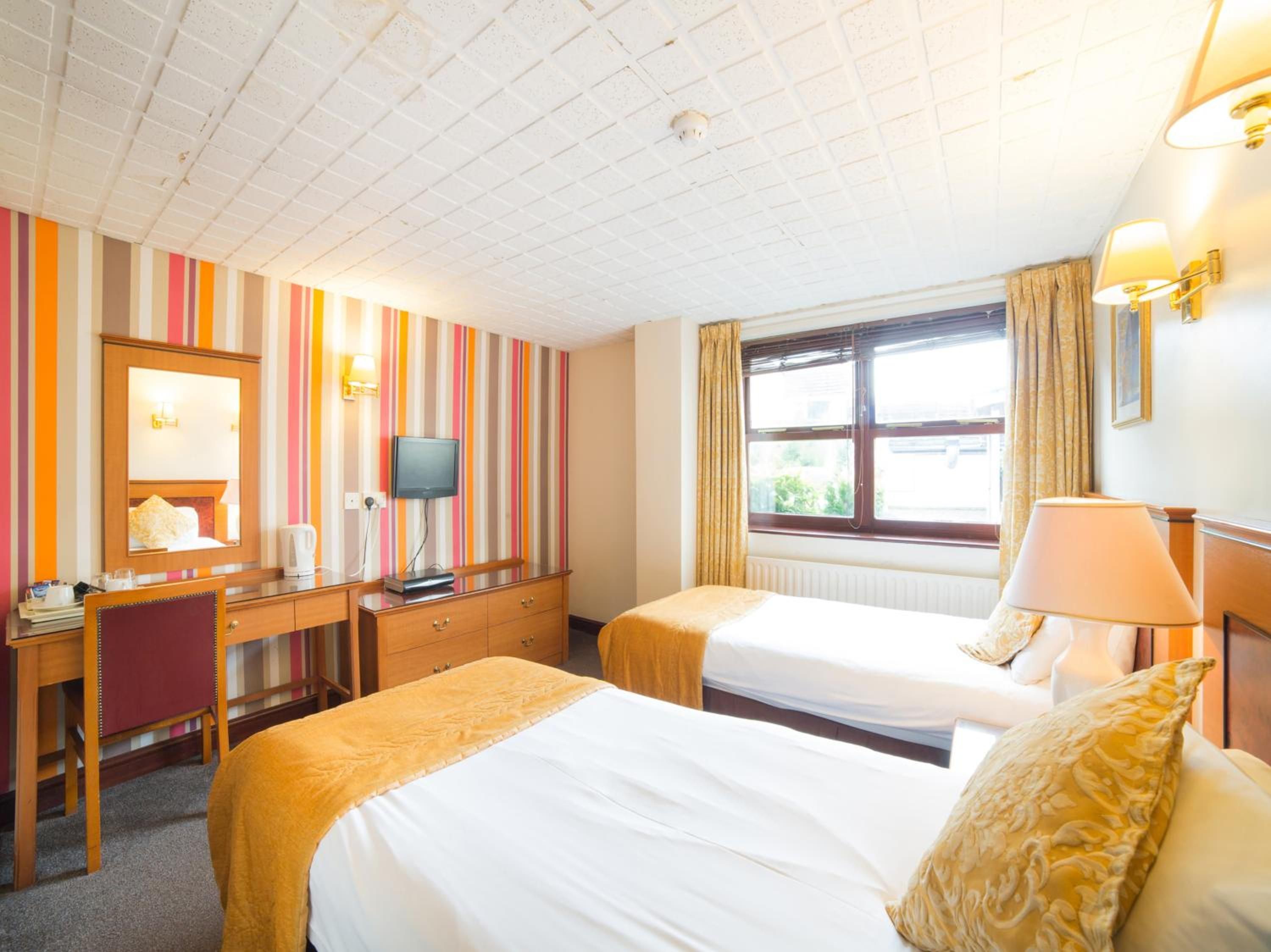A hotel room with two beds, a desk, a television, and a window with curtains.