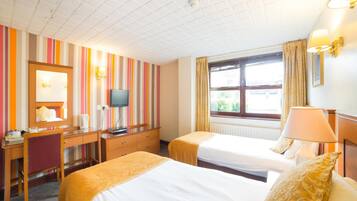 A hotel room with two beds, a desk, a television, and a window with curtains.