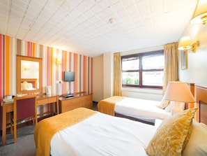Quarto de hotel com duas camas, uma escrivaninha, televisão e janela com cortinas.