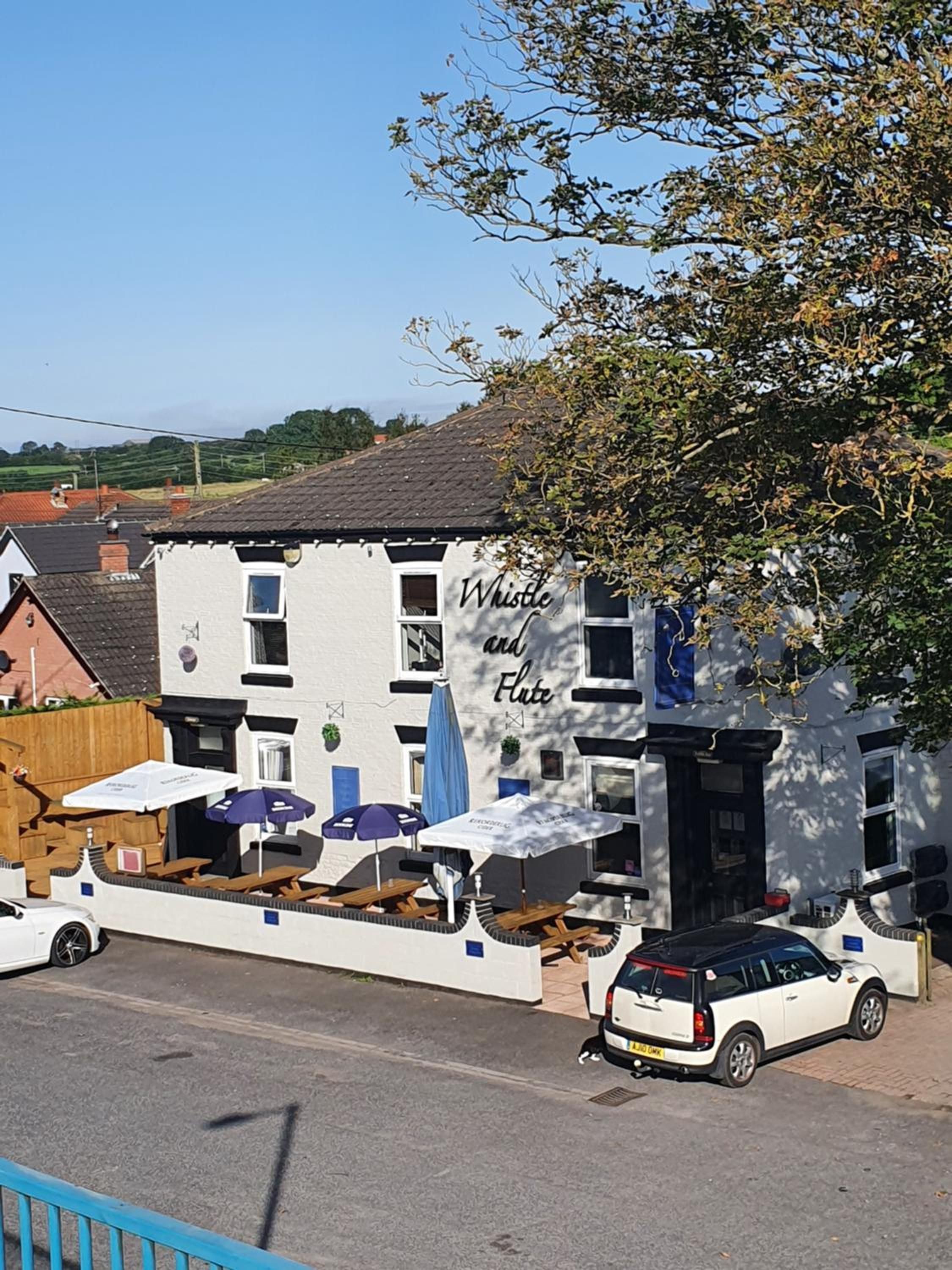 A building with a sign reading 'Whistle and Flute' and outdoor seating with umbrellas.