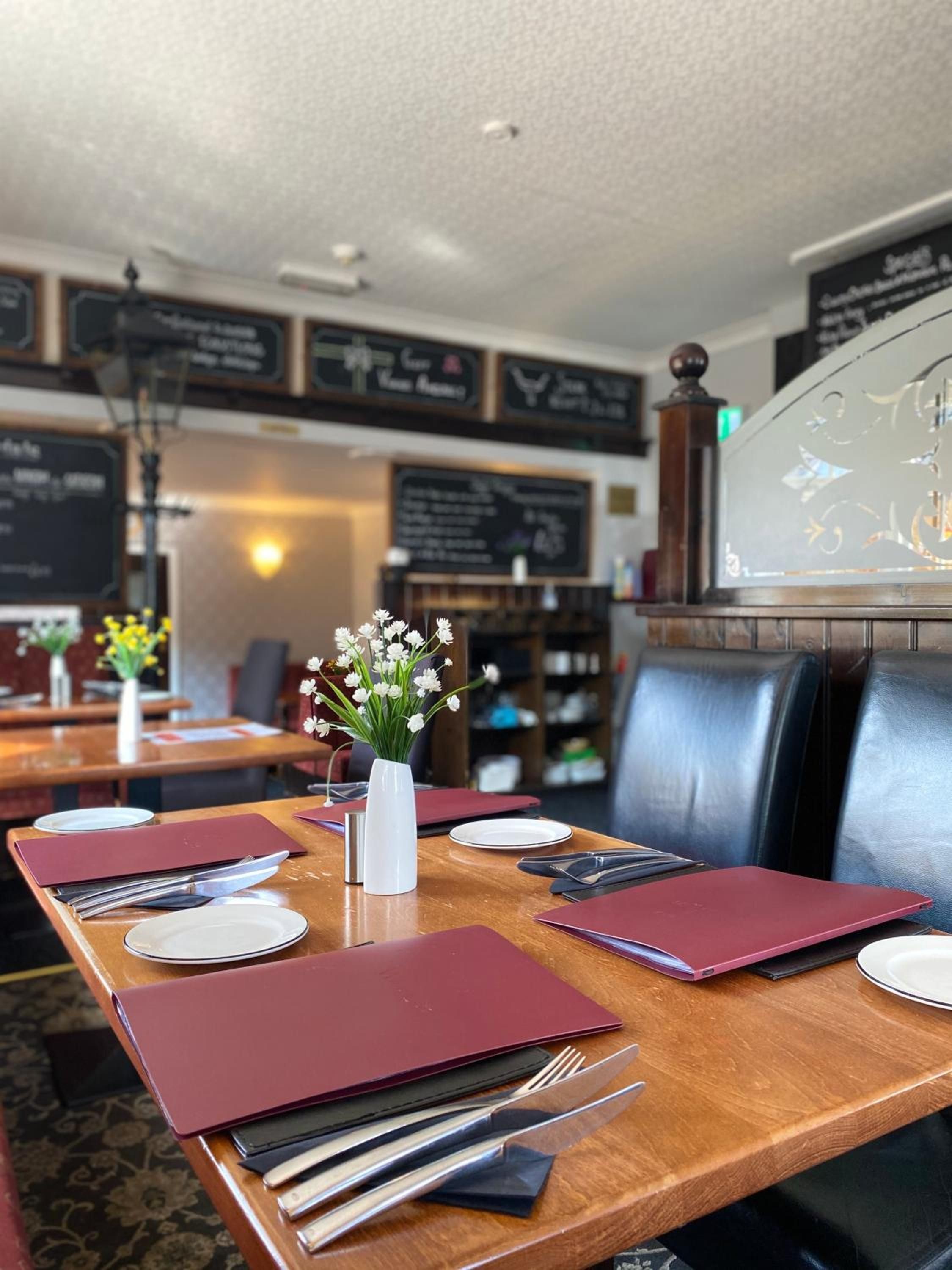 A restaurant setting with tables set for dining, menus, and a vase with flowers.