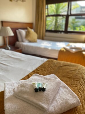 A hotel room with two beds, a window with a view of greenery, and a towel with toiletries on it. - The Whistle And Flute (Barnetby)
