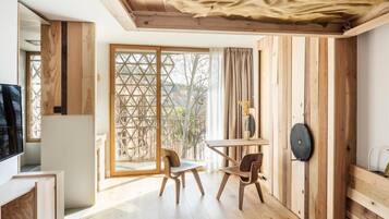 A room with a wooden floor, a table with chairs, a TV, and a large window with a view of the outside.