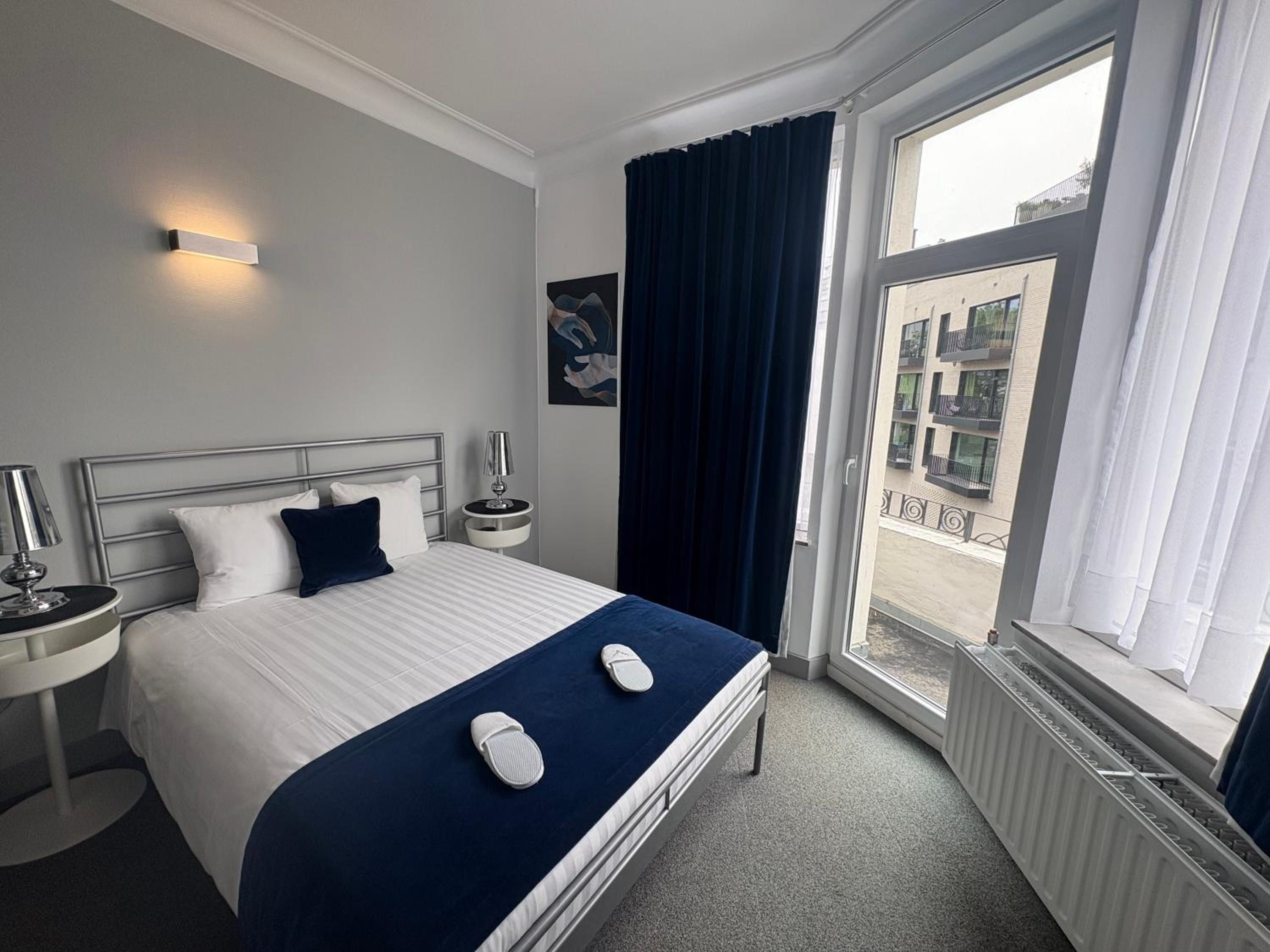 Une chambre d’hôtel avec un lit, une table de chevet, une lampe, une fenêtre avec des rideaux et une vue sur l’extérieur.