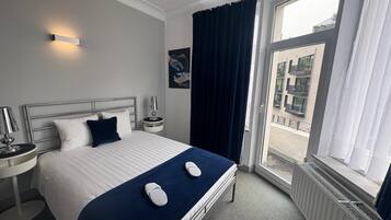 Une chambre d’hôtel avec un lit, une table de chevet, une lampe, une fenêtre avec des rideaux et une vue sur l’extérieur.